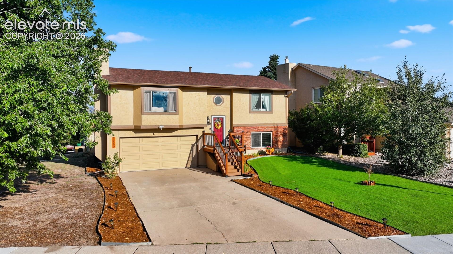 Split-level residence featuring a two-car garage, concrete driveway, and a red front door