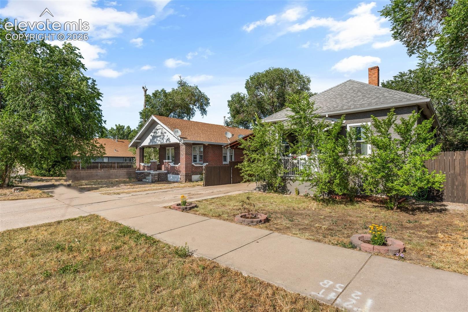 Traditional bungalow with grey siding, a front porch, and a brick chimney