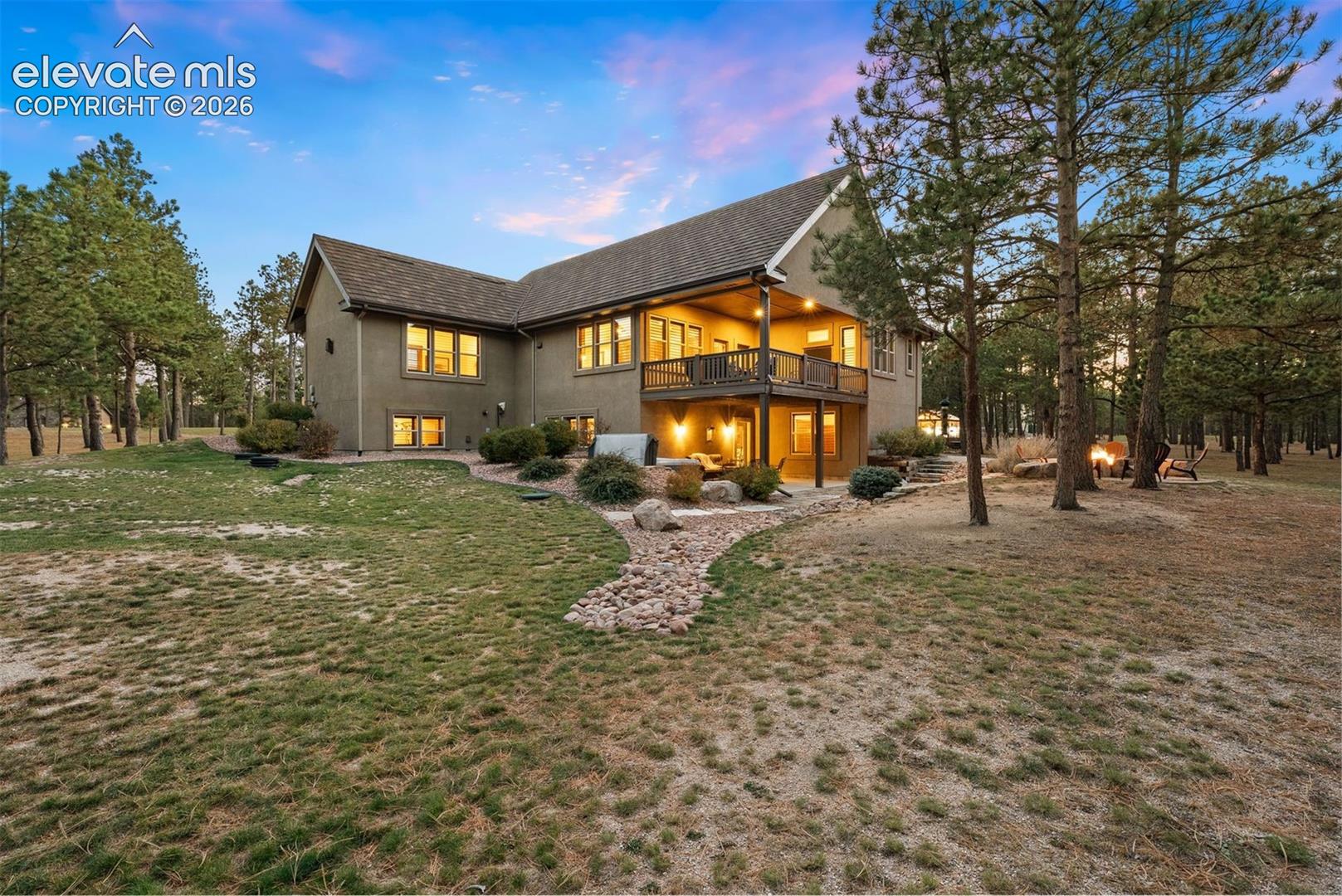 Exterior rear elevation featuring a multi-level deck, covered patio space, stucco siding, and surrounding mature evergreen trees
