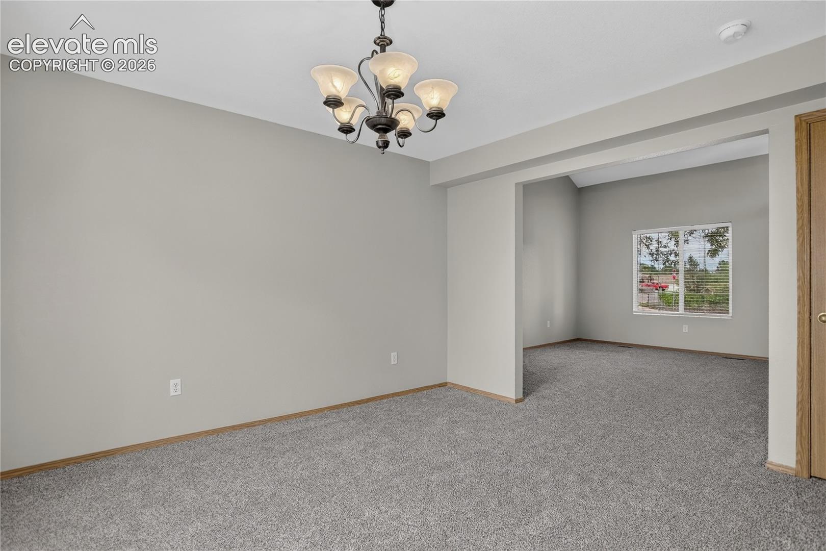 Recessed ceiling with an ornate chandelier, neutral tone walls, and gray carpeting