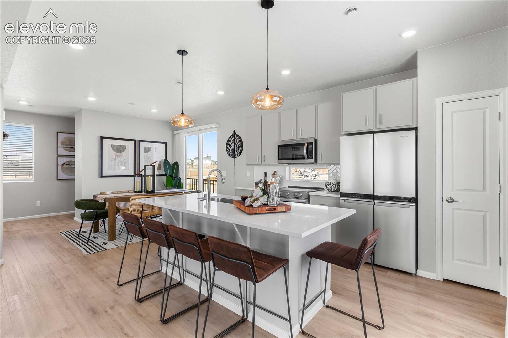 Open-concept kitchen and dining area featuring light-toned wood-finish flooring, a kitchen island with seating, stainless steel appliances, and white cabinetry
*photos of a model home*