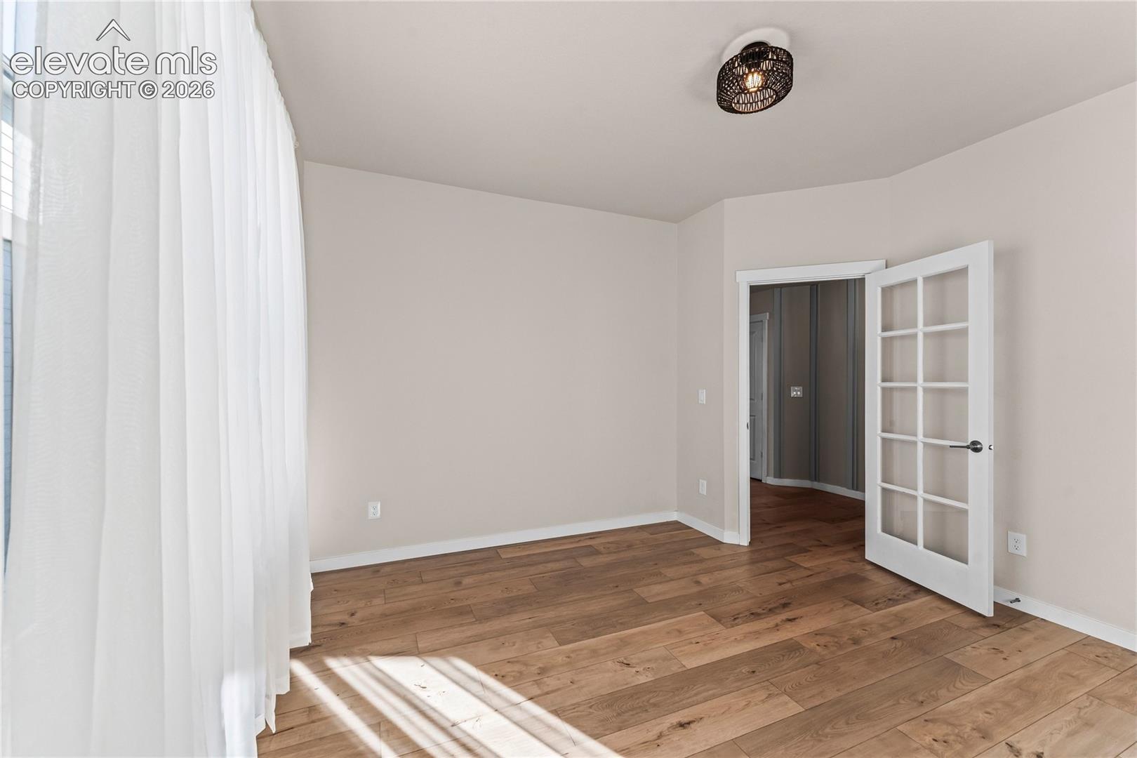 Interior space featuring wood-finish flooring, a white French door with glass panes, and a flush-mount drum ceiling light