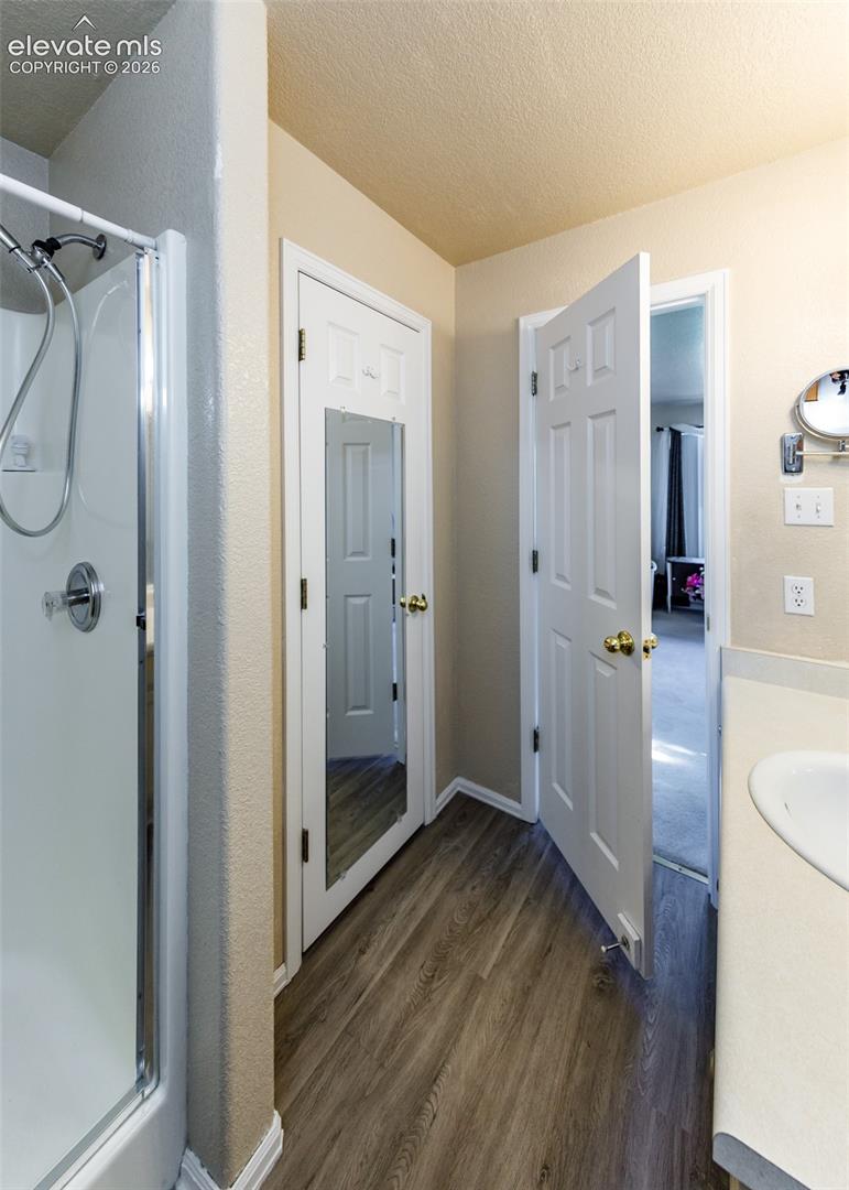 Shower enclosure with a metallic fixture, wood-finish flooring, and a mirrored door panel