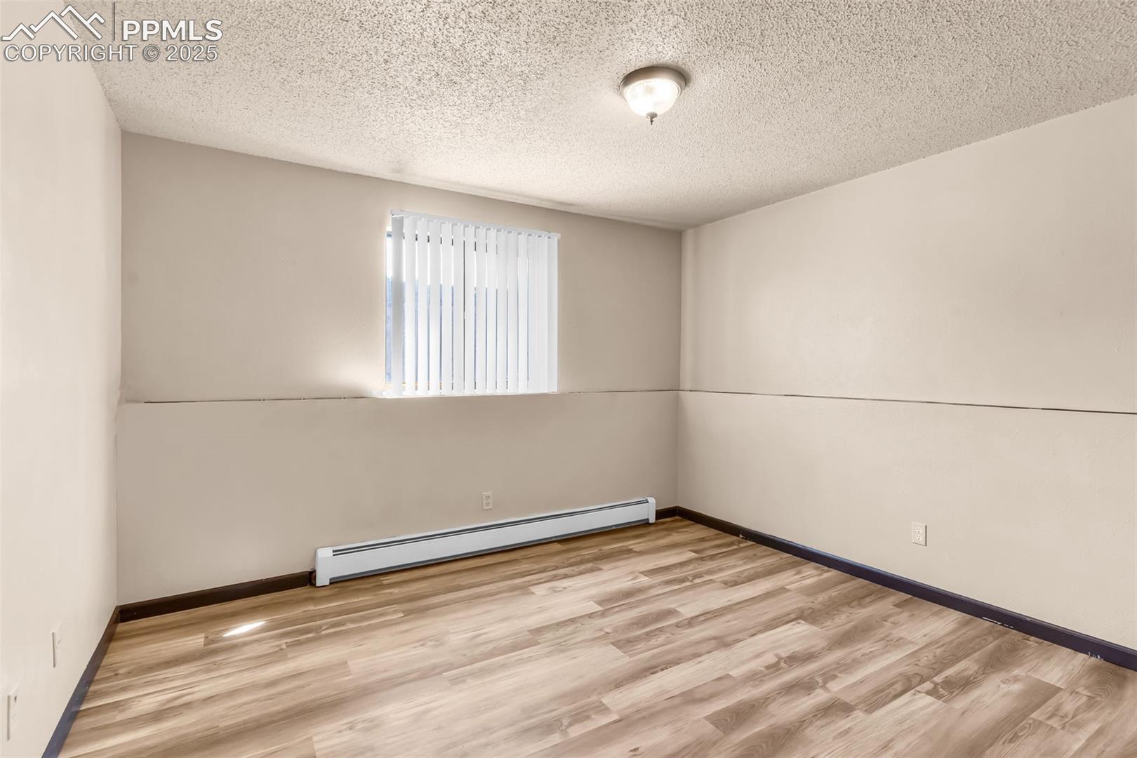 Spare room featuring baseboard heating, light wood-style floors, and a textured ceiling