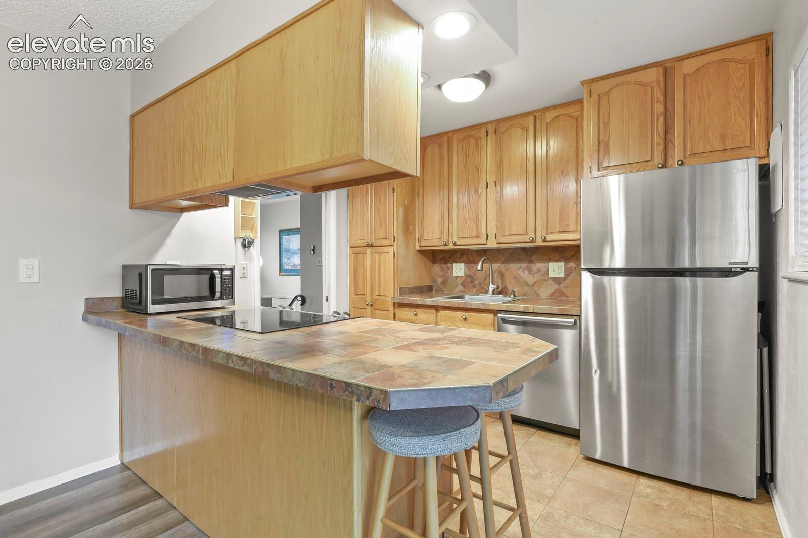 Kitchen featuring wood cabinetry, stainless steel appliances, a tile countertop, and a tile backsplash