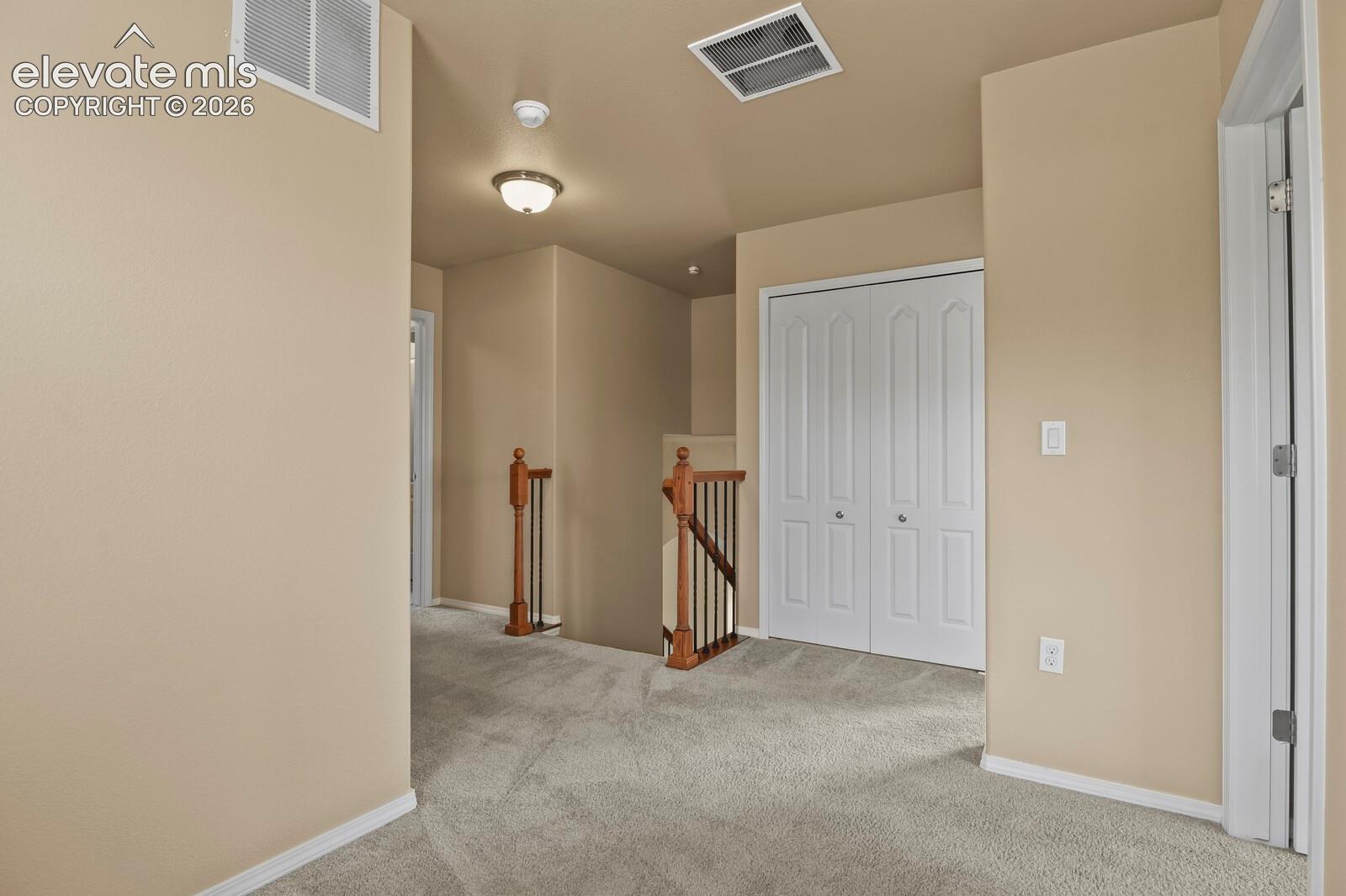 Neutral-toned carpet flooring, light beige wall paint, white bi-fold closet doors, and wood-finish stair railings