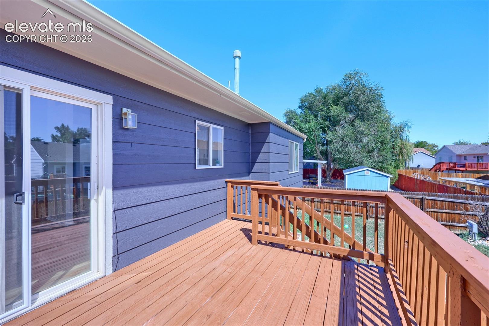 Expansive wood deck with wood railings, sliding glass door access, and exterior wall lighting