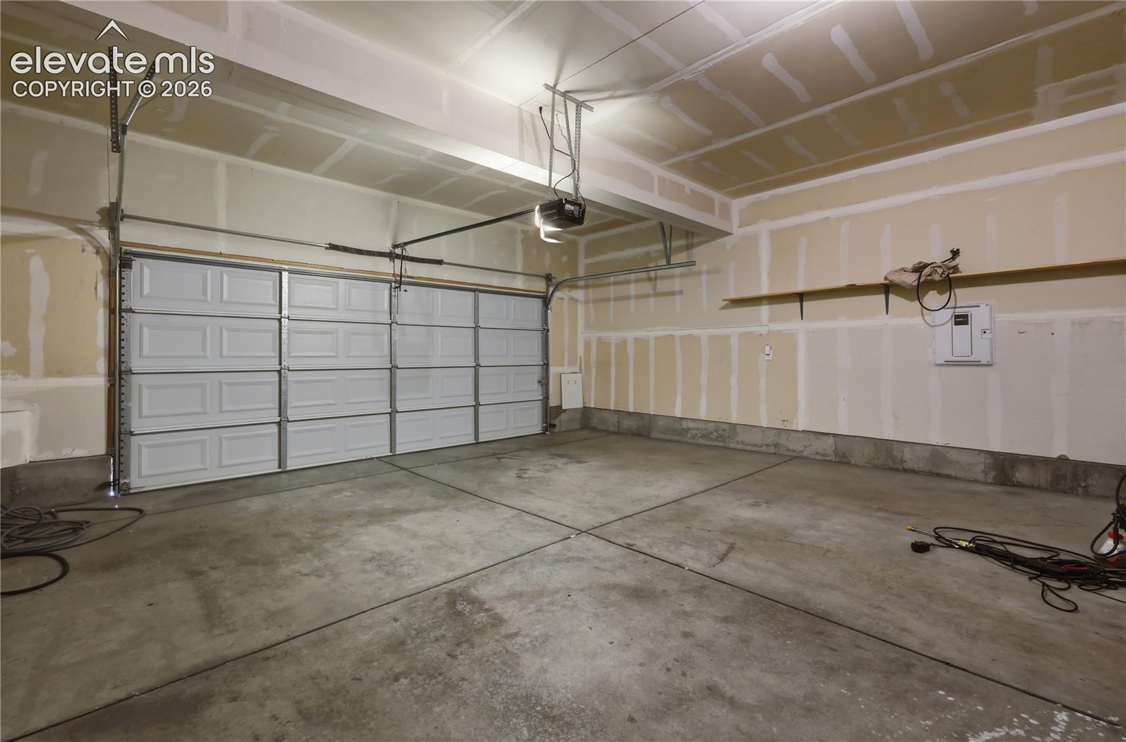Spacious garage featuring a concrete floor, overhead lighting, an automatic garage door opener, and a built-in wall shelf