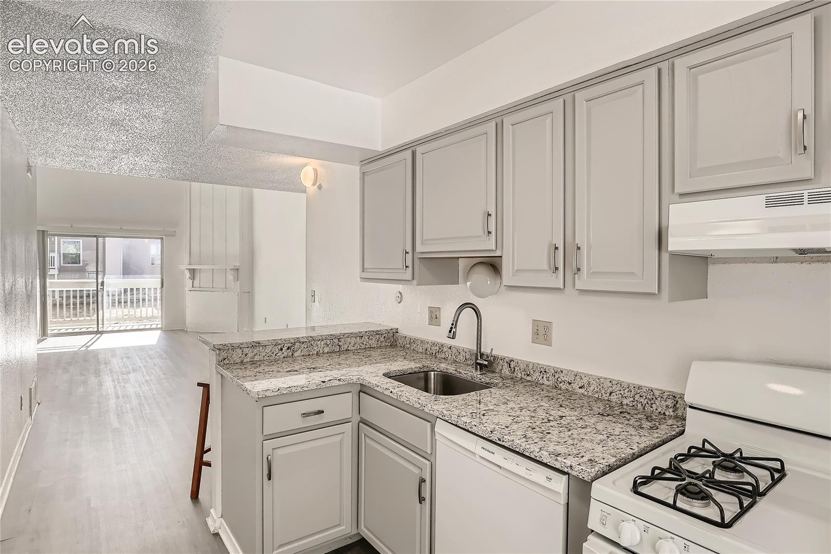 Kitchen featuring grey cabinetry, stone-finish countertops, stainless steel sink with a high-arc faucet, and light-tone wood-finish flooring