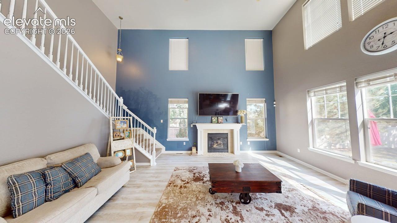 Two-story living space featuring high ceilings, a white-mantled fireplace, and light wood-finish flooring