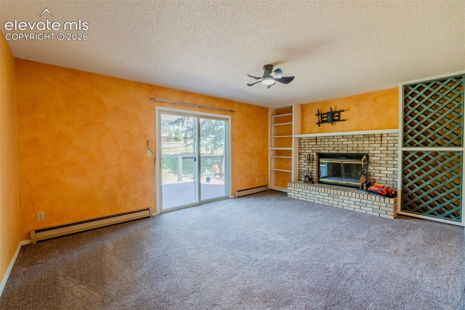Spacious room featuring a brick-surround fireplace, built-in shelving, glass sliding doors, and a ceiling fan