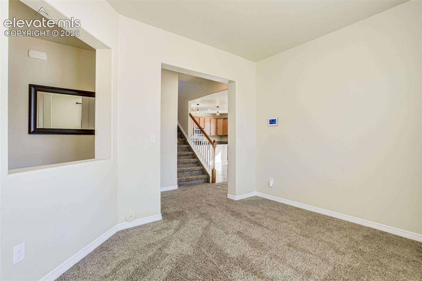 Carpeted living space with neutral wall paint and a staircase with white balusters