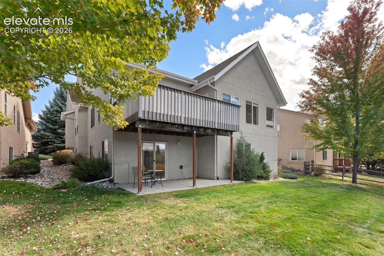 Two-story exterior featuring a stucco facade, an elevated wood deck with lattice railing, a concrete ground-level patio, and a grass-covered backyard