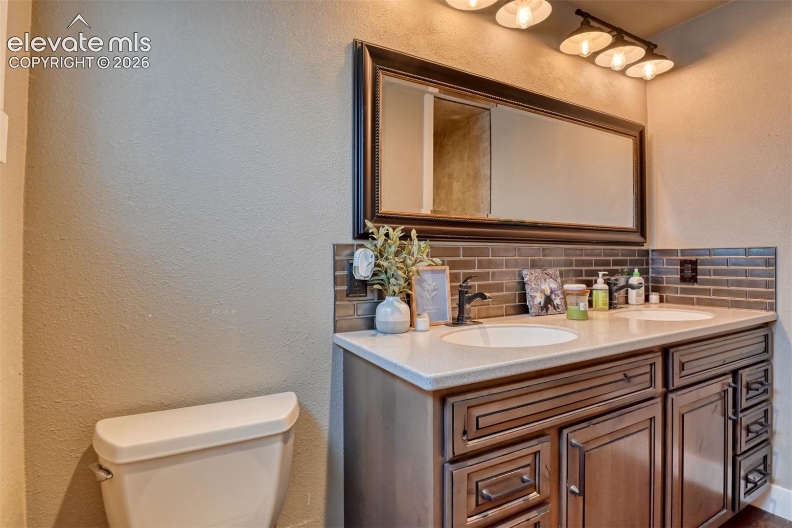 Full bath featuring a textured wall, double vanity, and decorative backsplash