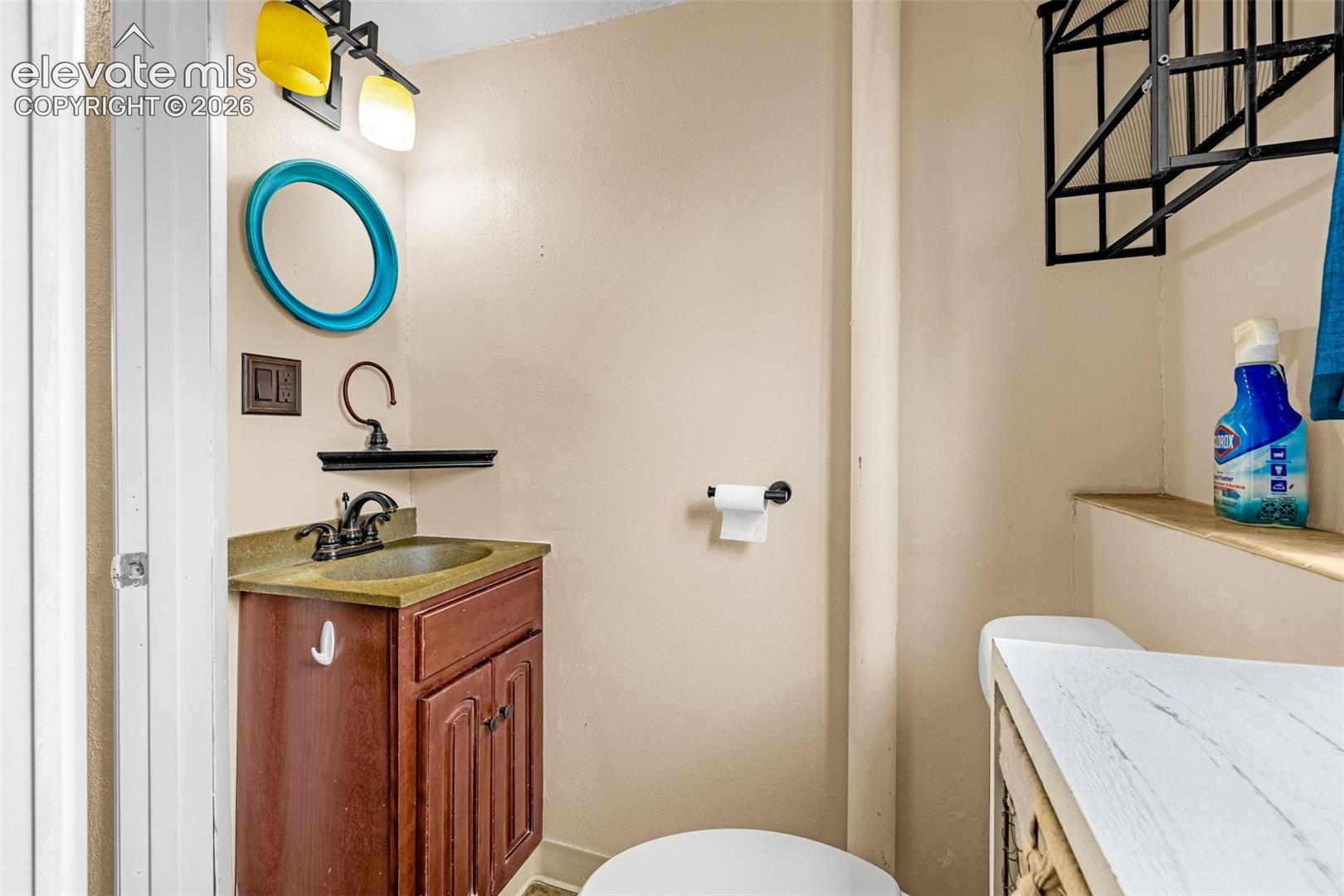Wood-finish vanity with a stone-composite surface, oil-rubbed bronze faucet, integrated wall shelf, and multi-light fixture