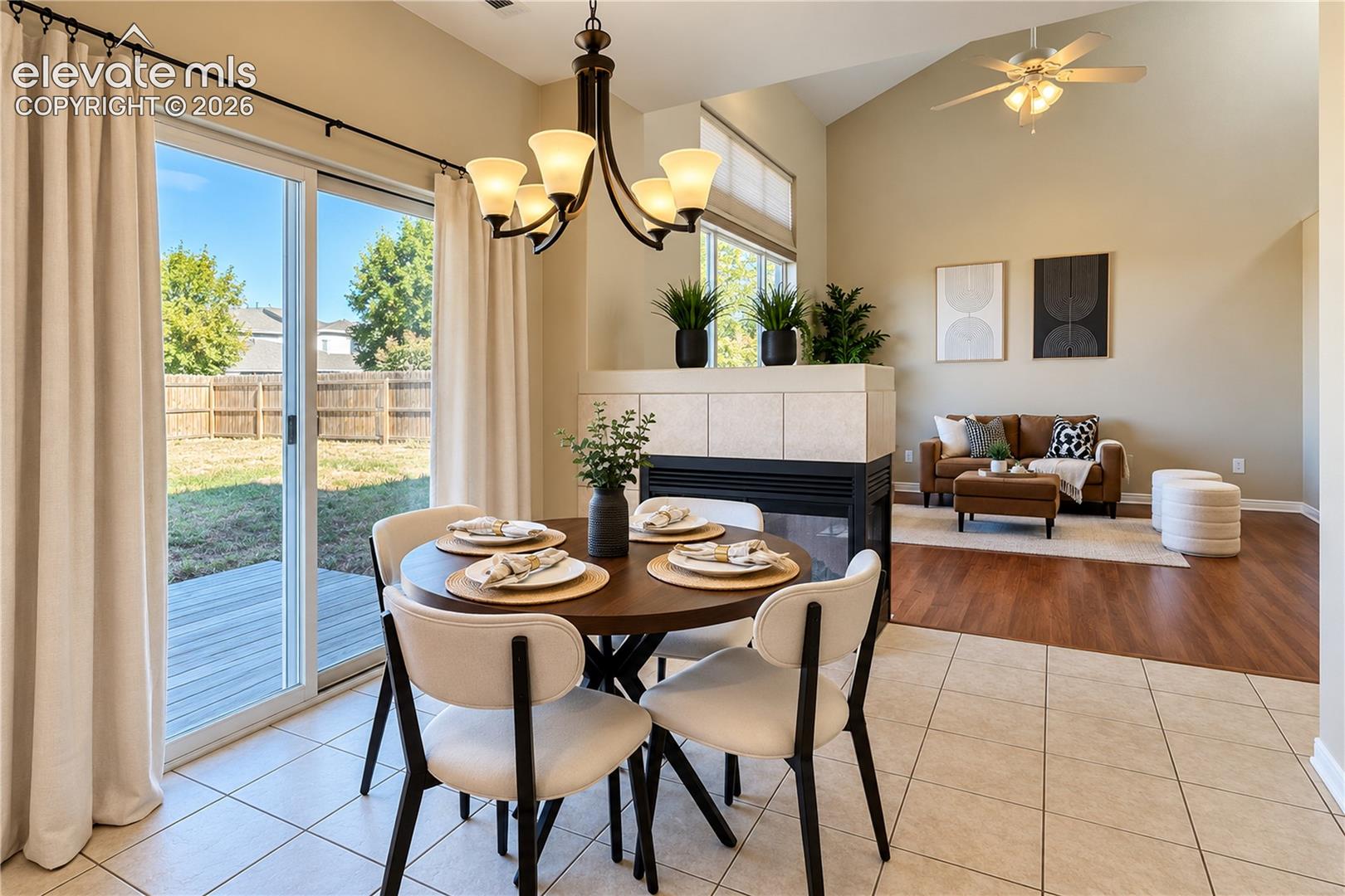 Vaulted ceiling with integrated ceiling fan, dual-sided fireplace with tile surround, wood-finish flooring, and sliding glass door
