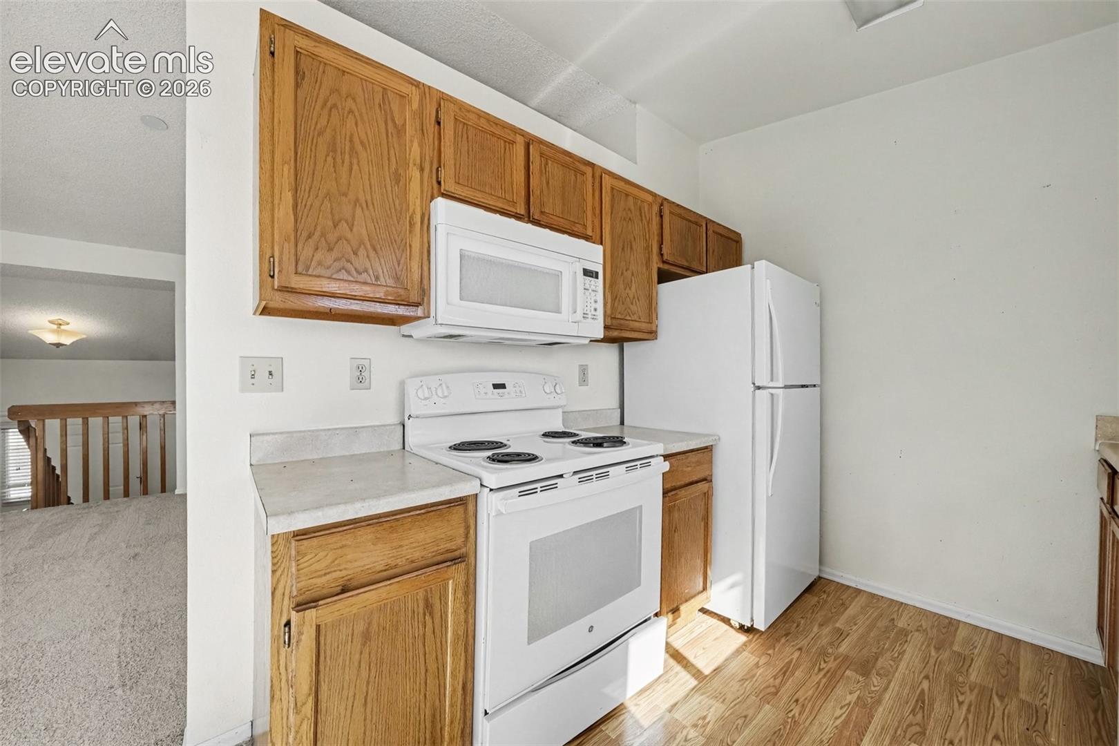 Kitchen featuring wood cabinetry, white appliances, and wood-finish flooring