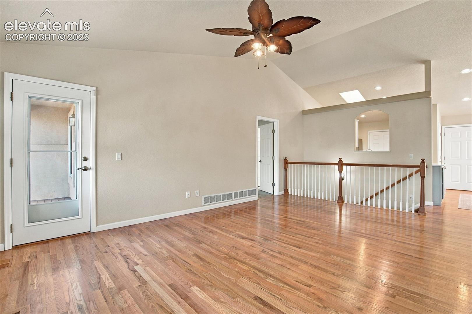 Vaulted ceiling featuring a palm-leaf style ceiling fan, wood-finish flooring, skylight, and white baluster railing