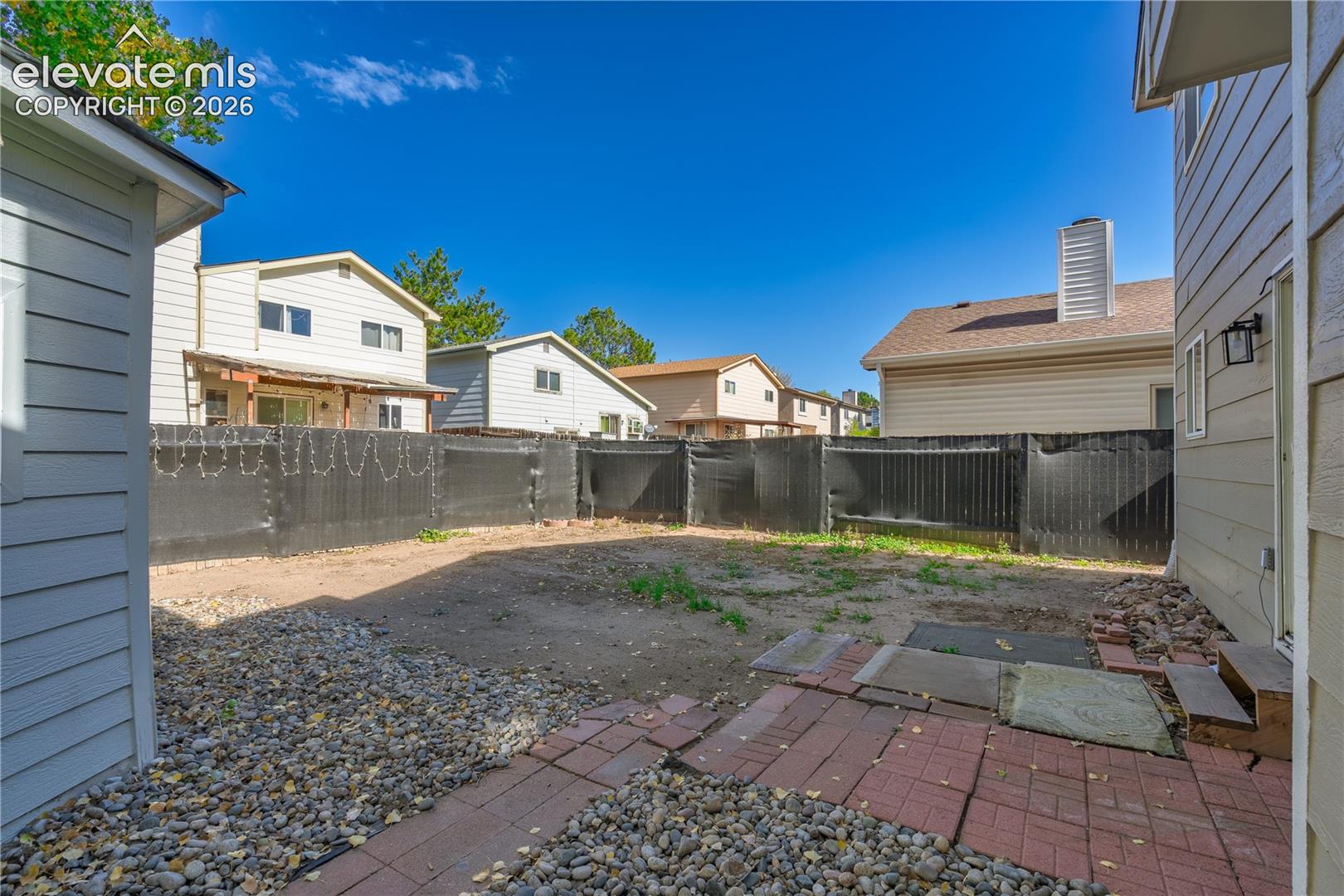Fenced exterior yard featuring a brick paver patio and decorative rock ground cover