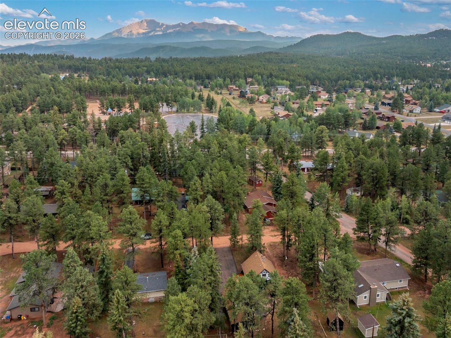 Mountain backdrop, expansive forested landscape, residential area, distant body of water, scattered structures