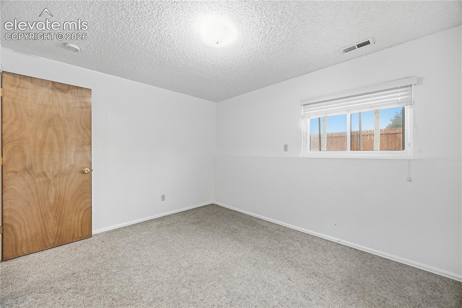 Interior room featuring wall-to-wall carpeting, a natural wood-finish interior door, and a horizontal sliding window with attached blinds