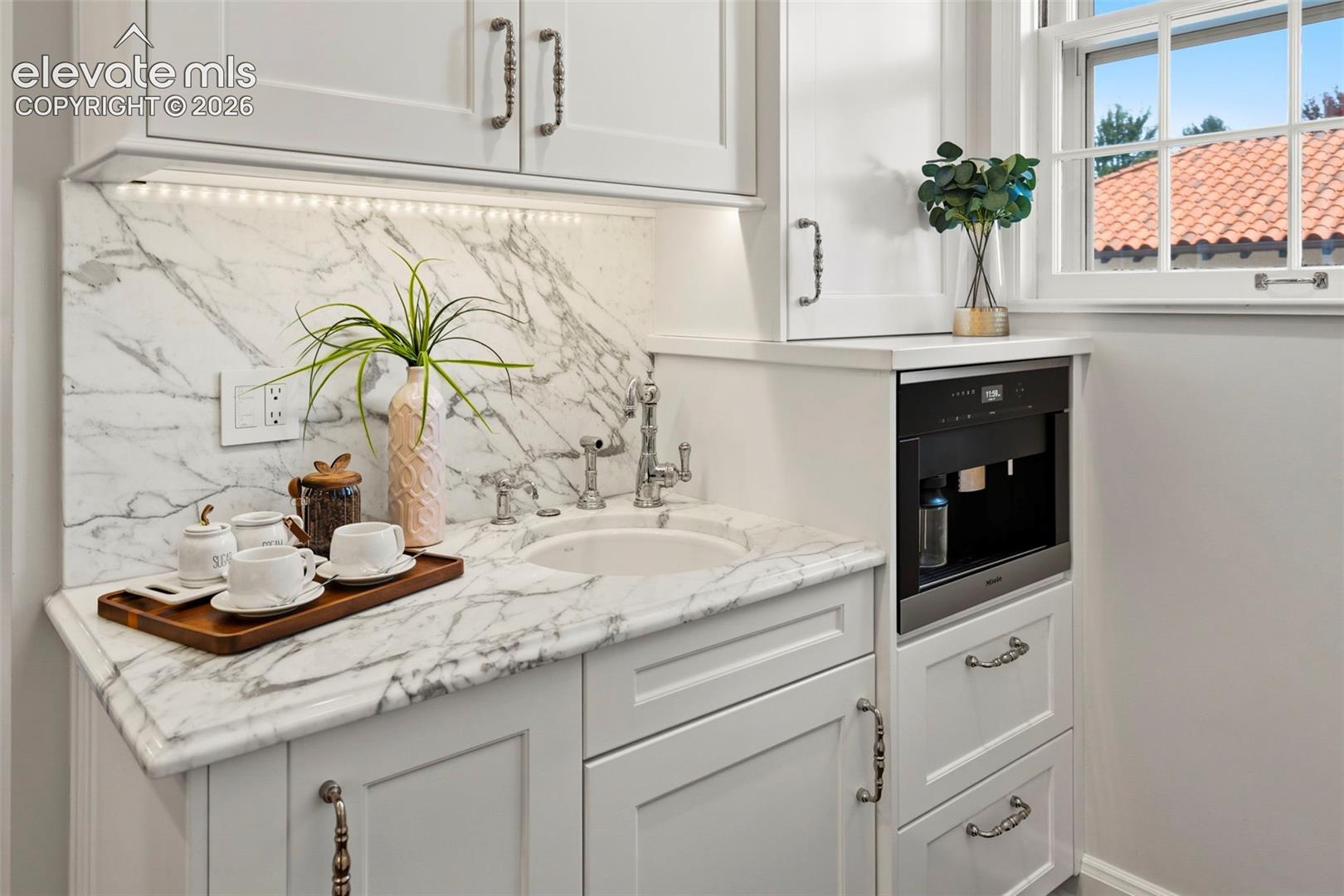 Custom cabinetry featuring integrated lighting and metallic hardware, stone countertop and backsplash, under-mount circular sink, and built-in coffee station