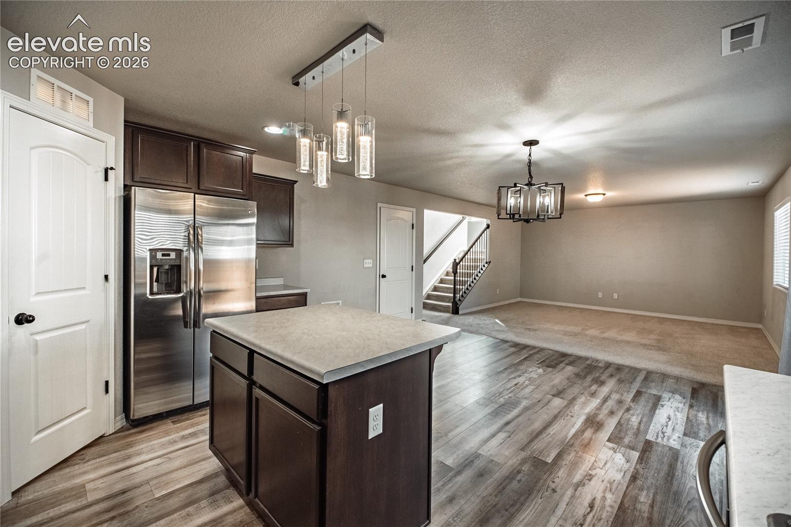 Kitchen island with solid surface countertop, wood-finish flooring, stainless steel refrigerator, dark wood cabinetry, and a modern chandelier