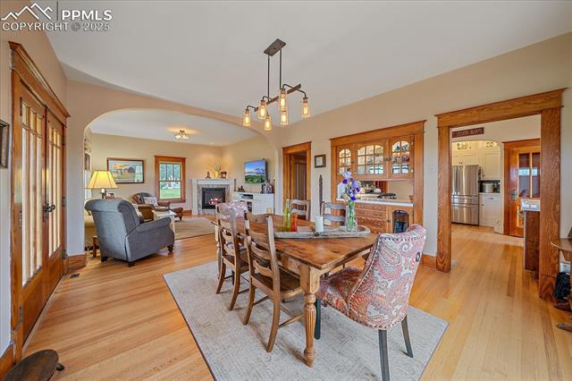 Dining space with arched walkways, light wood-style flooring, and a lit fireplace