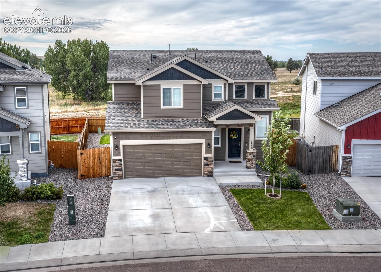 Two-story residence featuring horizontal siding, a multi-gabled roofline, stone veneer accents, an attached two-car garage, and a concrete driveway