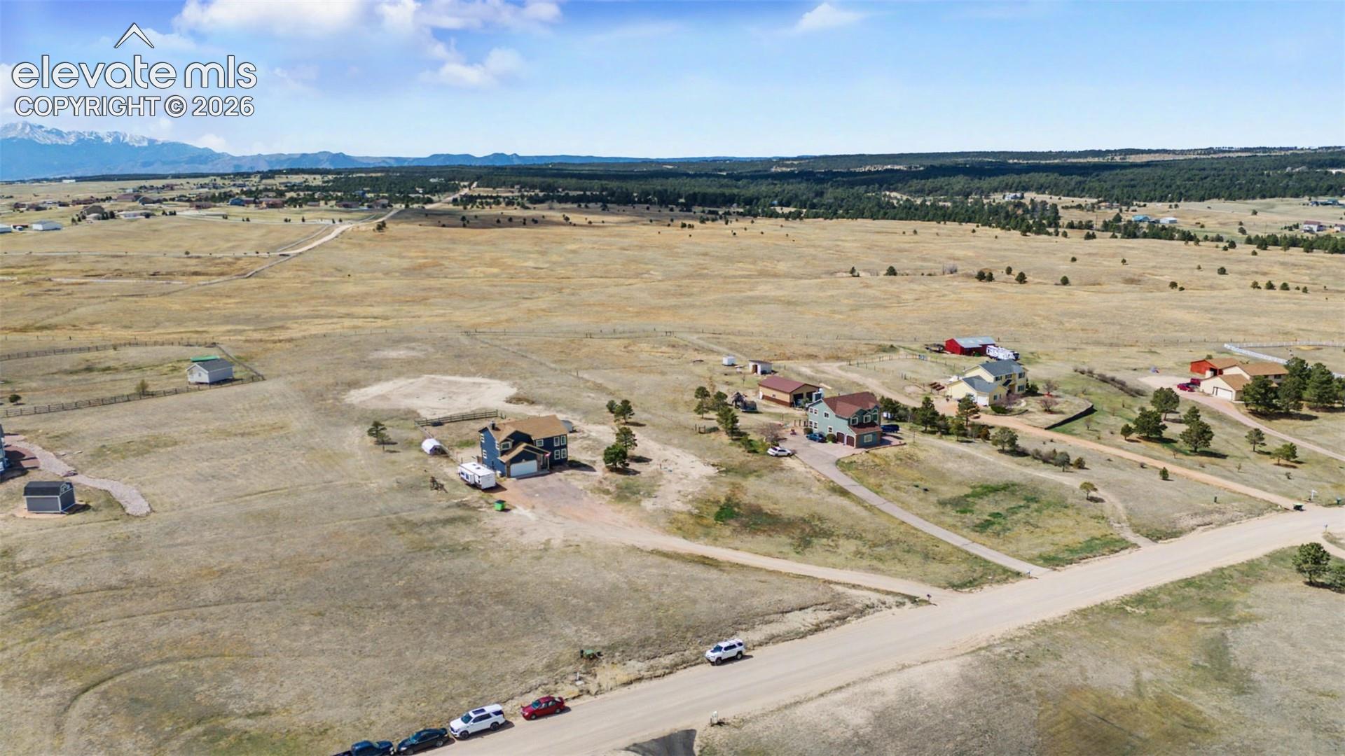 Aerial perspective featuring expansive acreage, a multi-story residence, secondary outbuildings, and a prominent mountain range backdrop