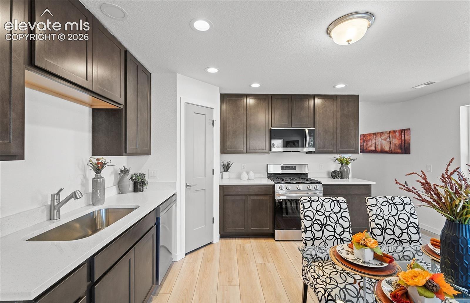 Kitchen featuring dark wood-finish cabinetry, solid-surface countertops, a stainless steel undermount sink, gas range with integrated microwave, and wood-finish flooring