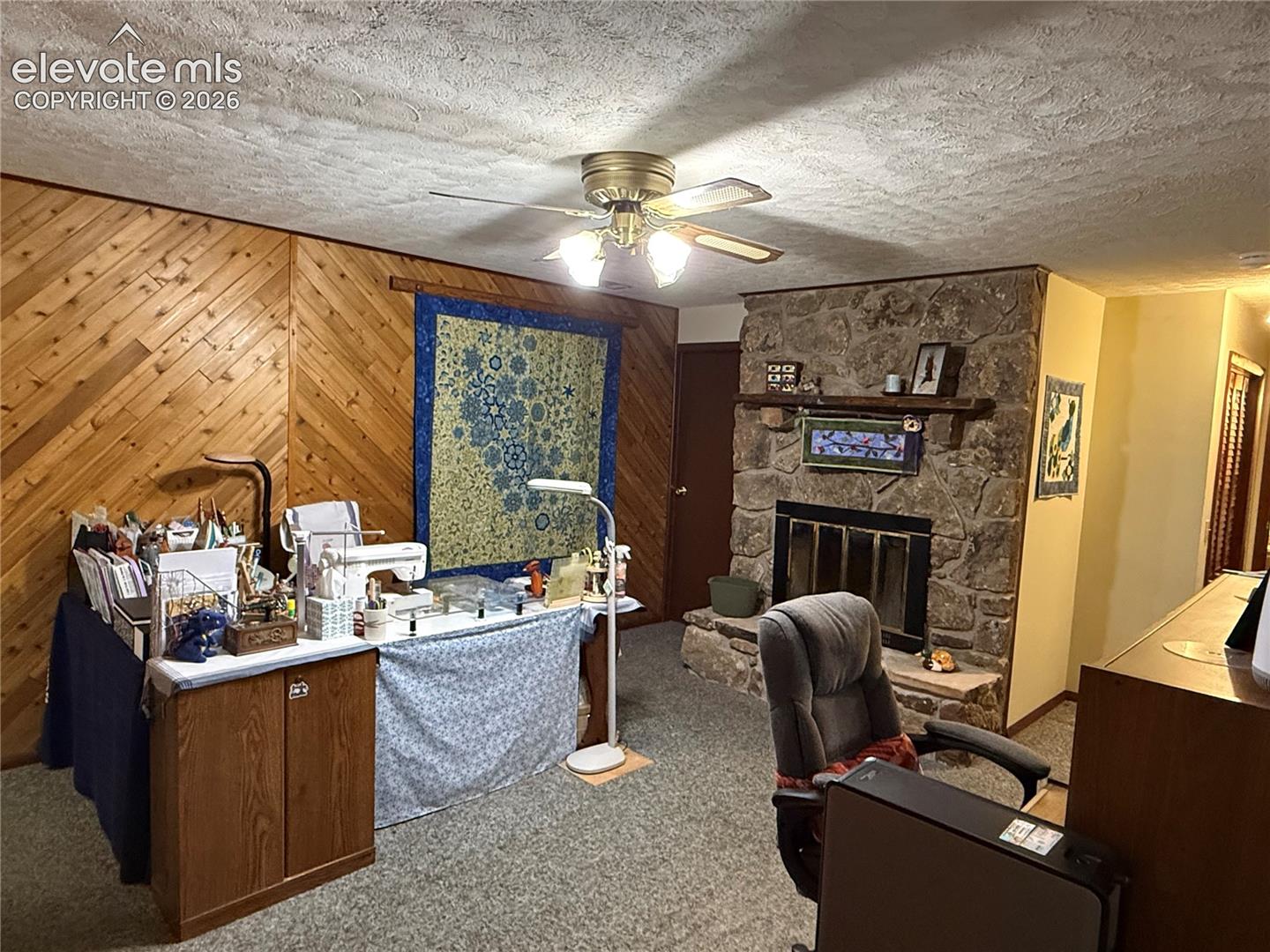 Living area featuring a stone-faced fireplace with a wood mantle, wood plank accent wall, and a textured ceiling