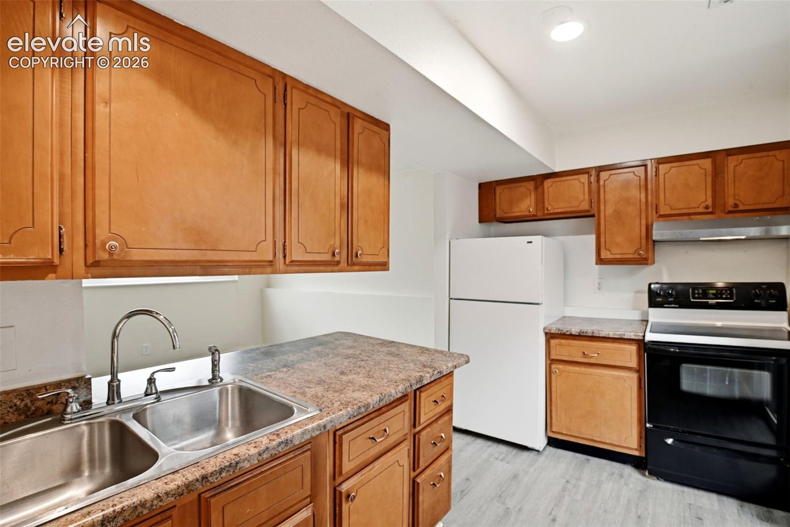 Kitchen featuring wood cabinetry, laminate countertops, a double basin stainless steel sink, black electric range, and a white refrigerator