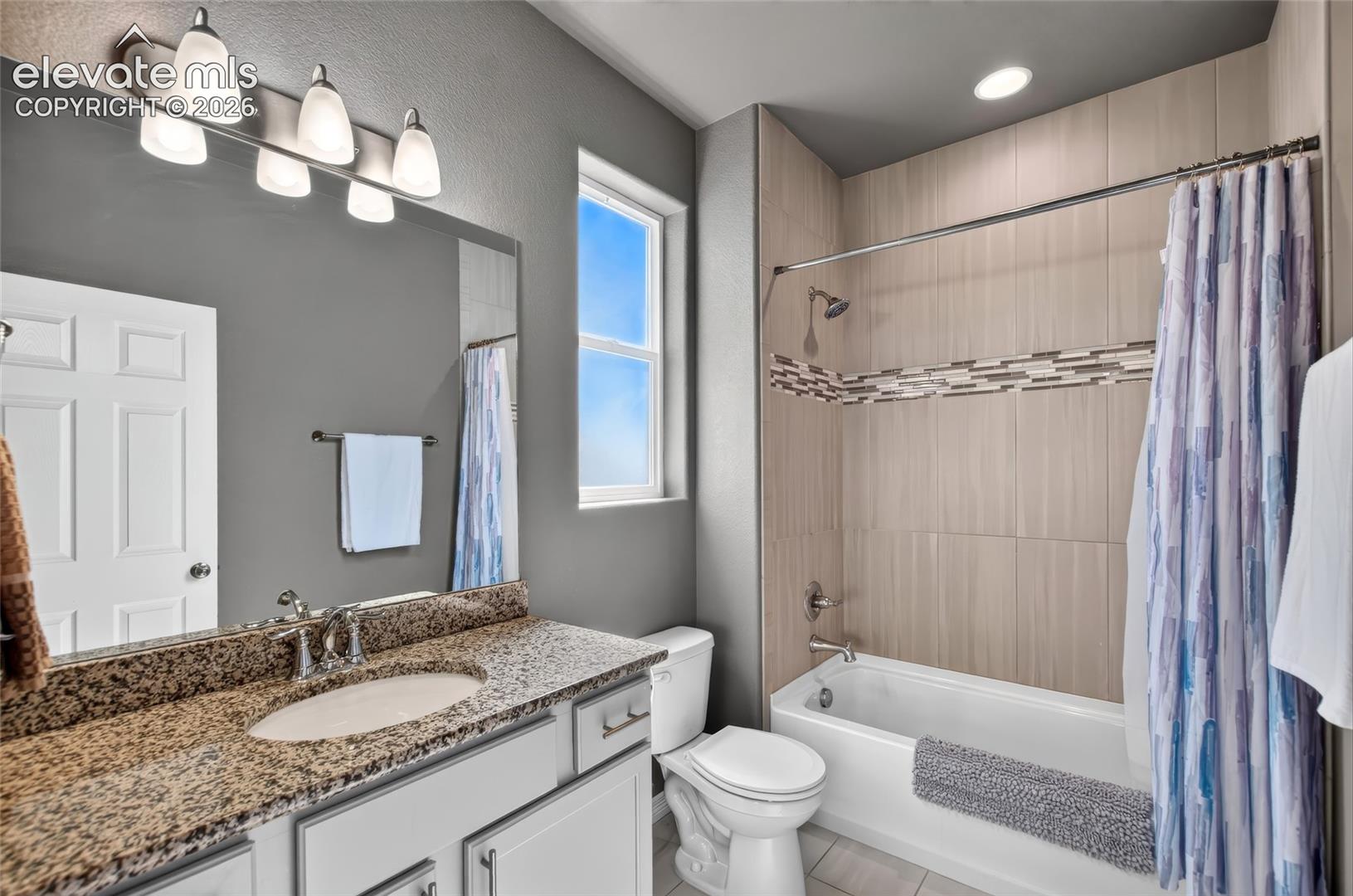 Bathroom featuring a vanity with a granite-style countertop, undermount sink, and white cabinetry