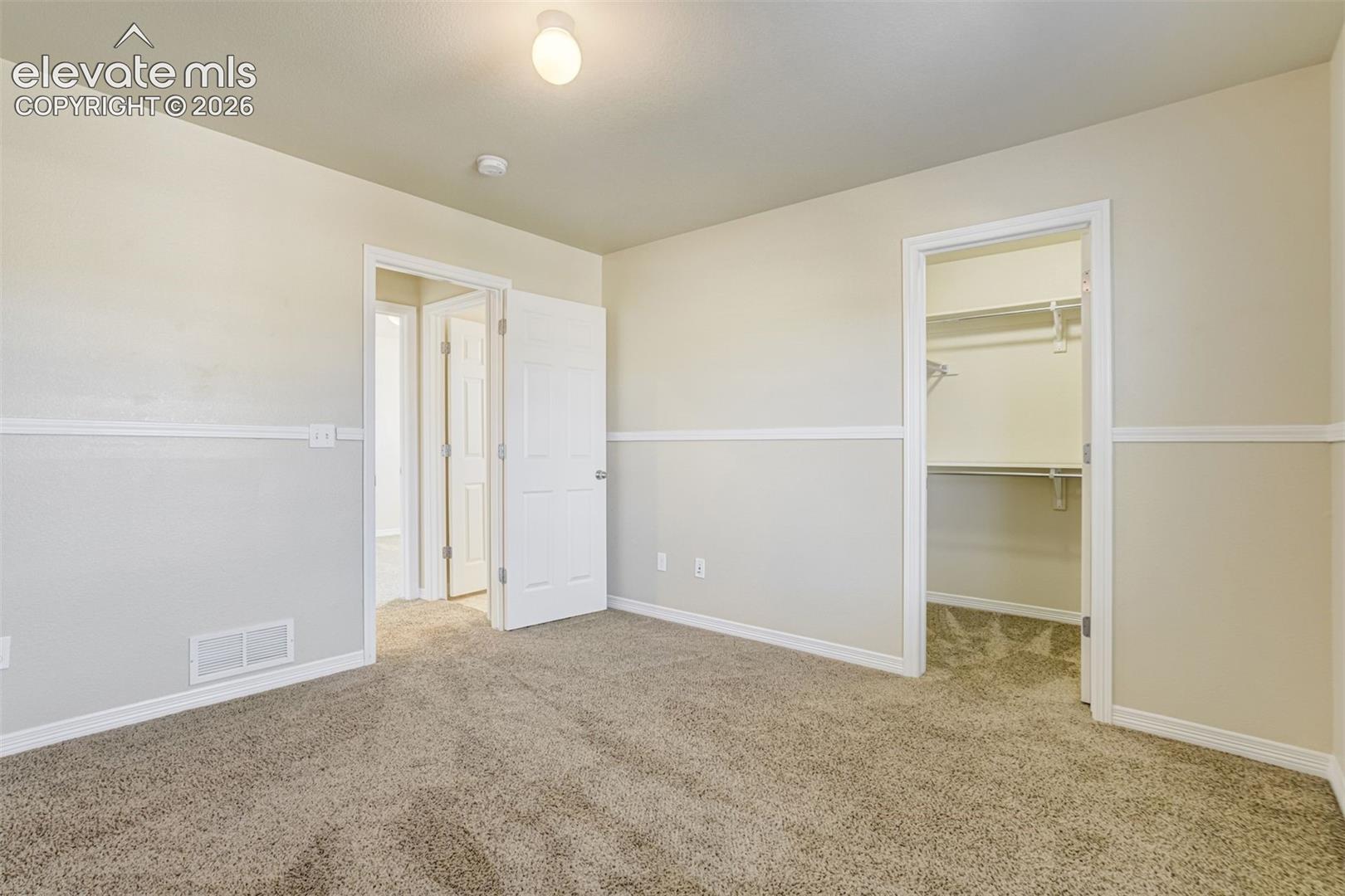 Secondary Bedroom. Carpeted room with neutral wall tones and white trim and a walk in closet.