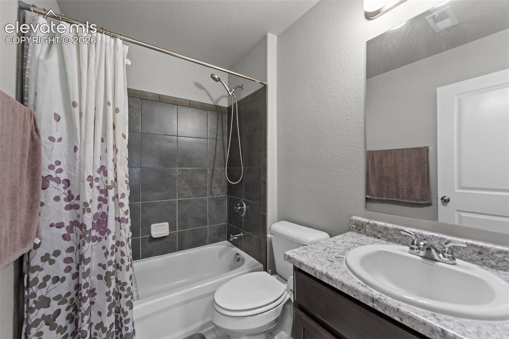 Bathroom featuring a bathtub with dark tiled surround, white toilet, vanity with integrated sink, and a speckled countertop