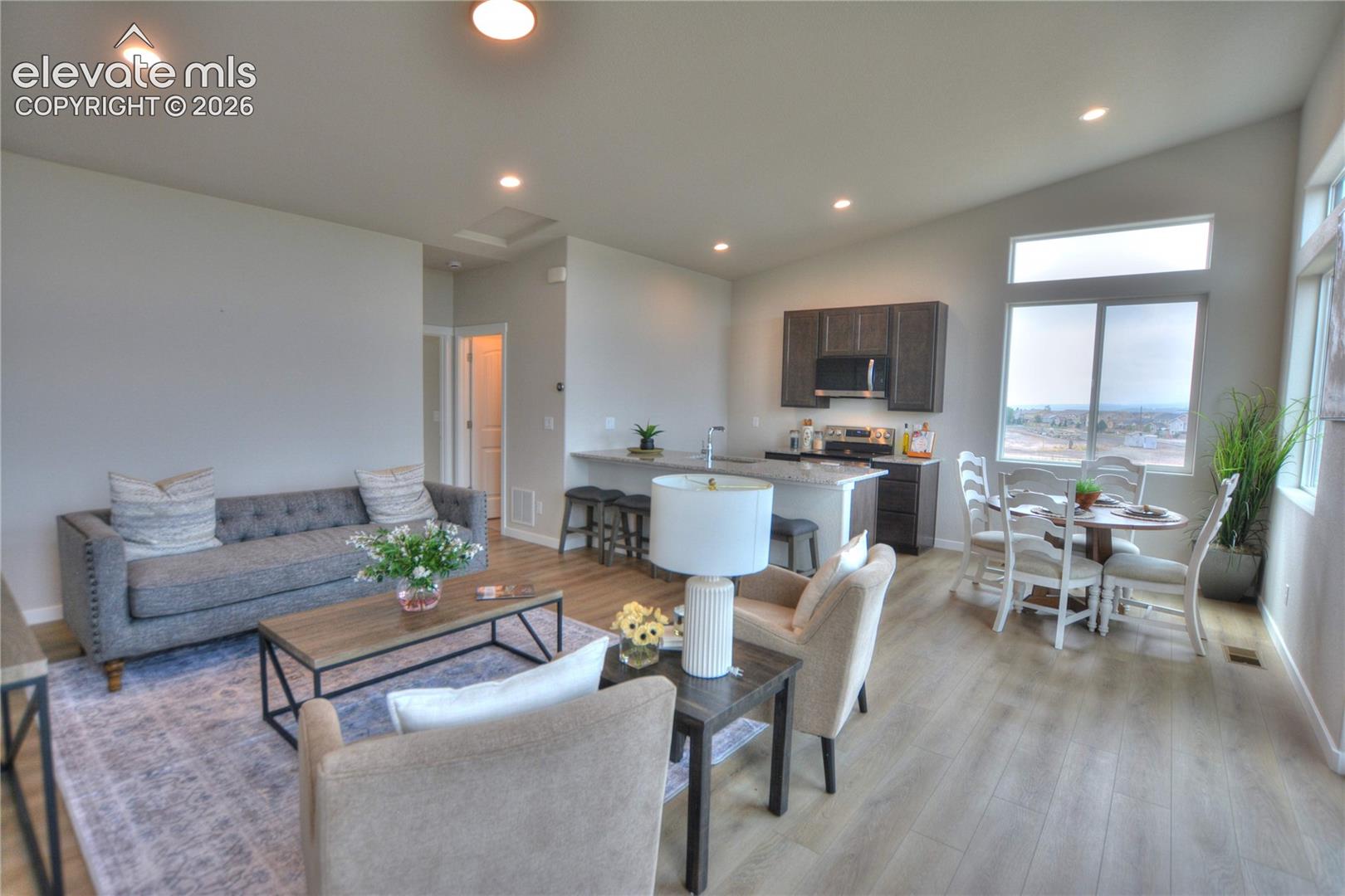 Open-concept living area with wood-finish flooring, recessed lighting, and large windows