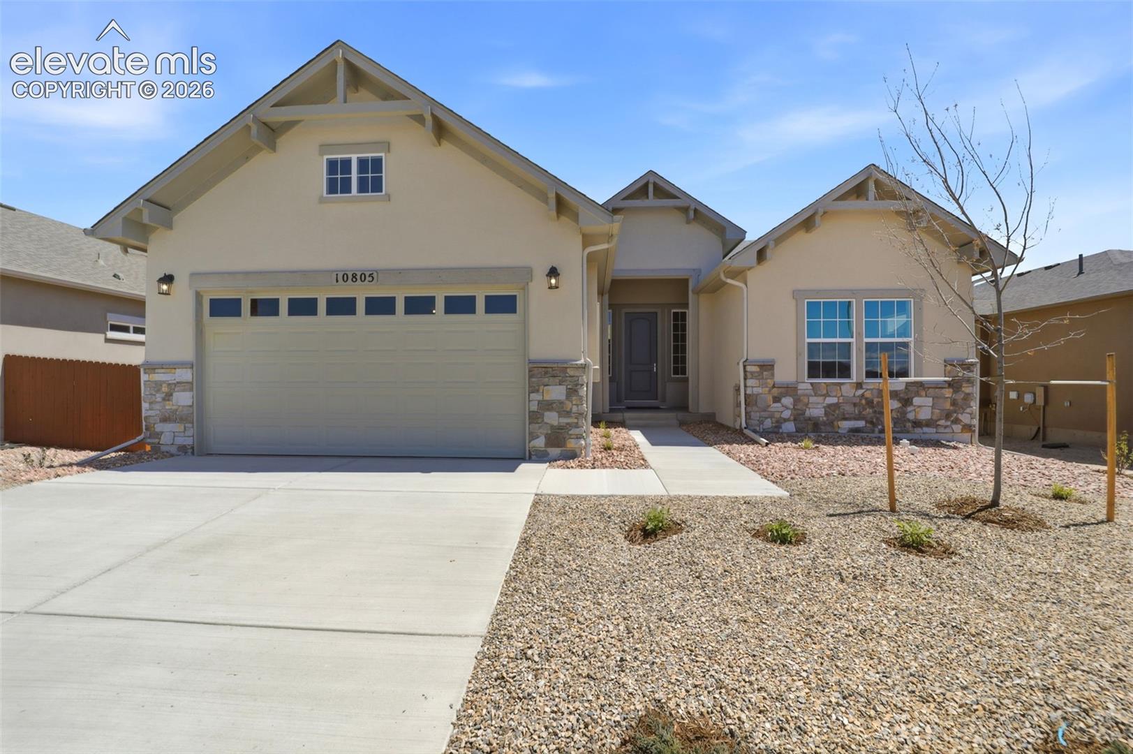 Single-story residence featuring a stucco and stone veneer facade, gabled rooflines with decorative brackets, an attached two-car garage, and a xeriscaped front yard