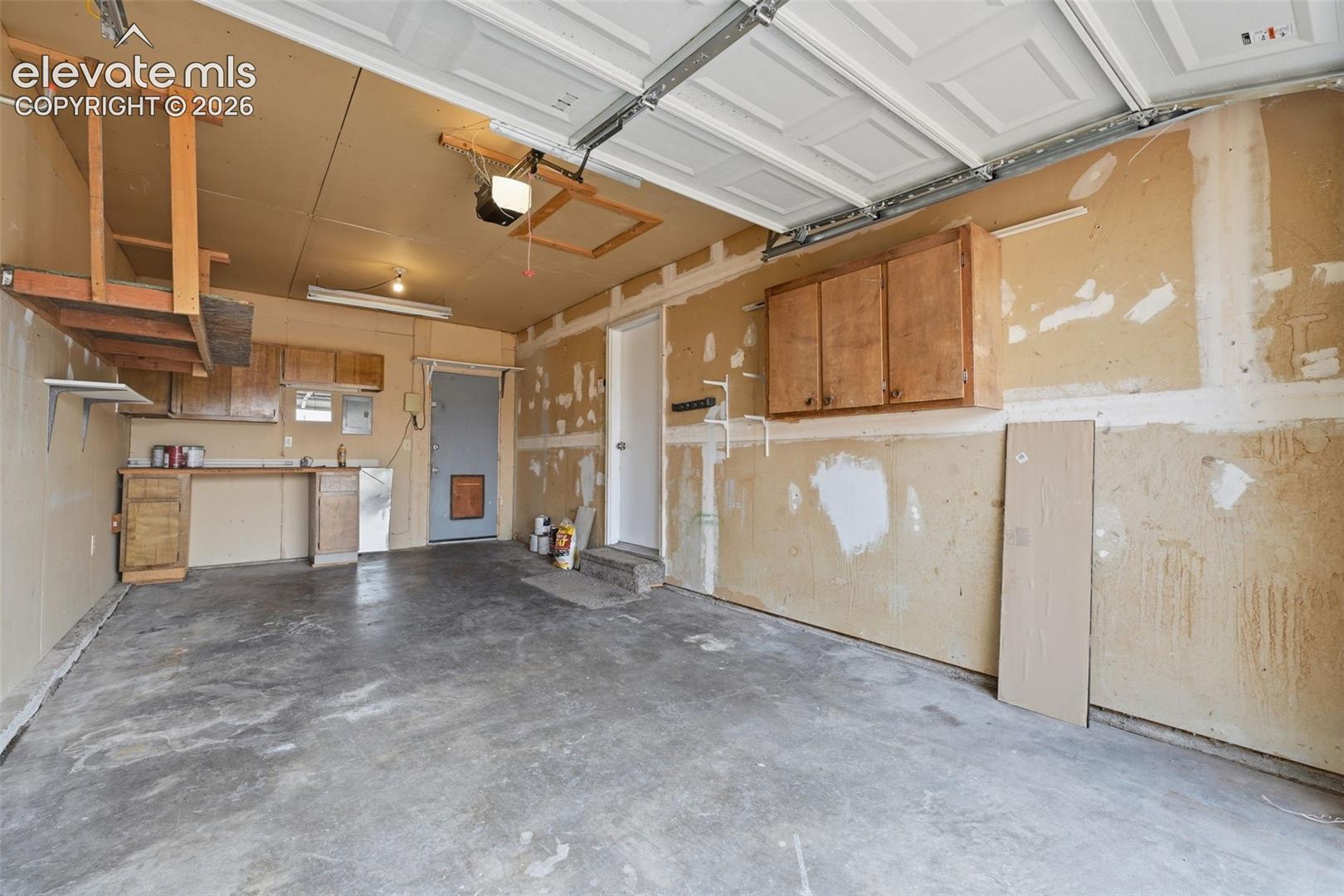 Attached overhead garage door, built-in cabinetry, concrete flooring, utility sink, and overhead storage shelving