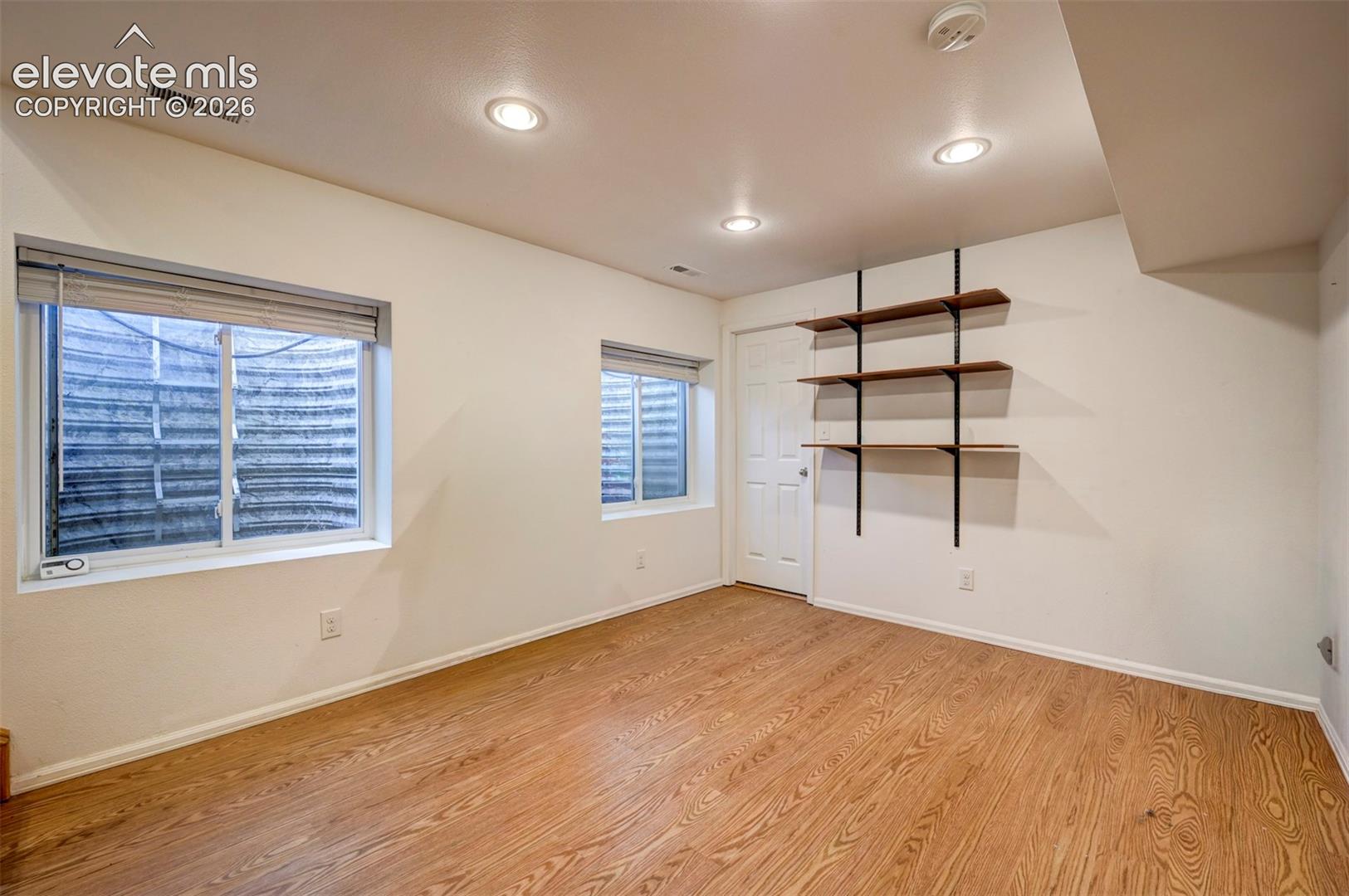 Wood-finish flooring, recessed ceiling lighting, built-in shelving, white paneled door, and two windows