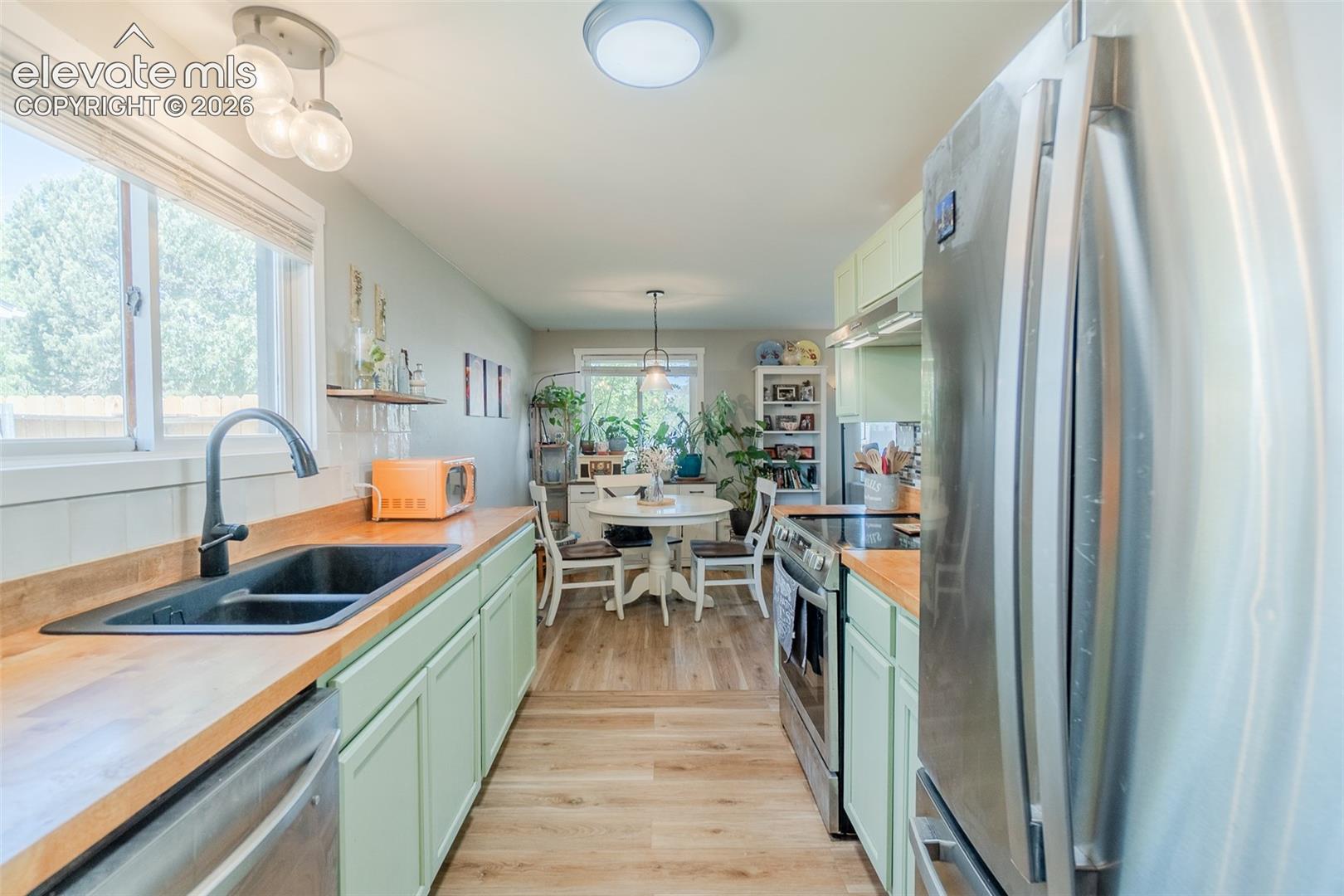 Kitchen featuring light green cabinetry, wood-finish countertops, and stainless steel appliances