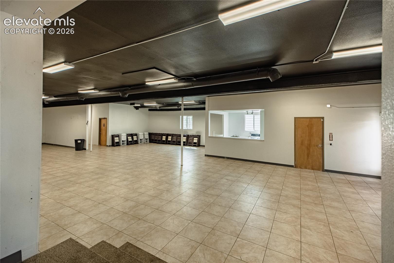 Expansive open-concept room featuring tiled flooring, a suspended ceiling with fluorescent lighting, and a service window