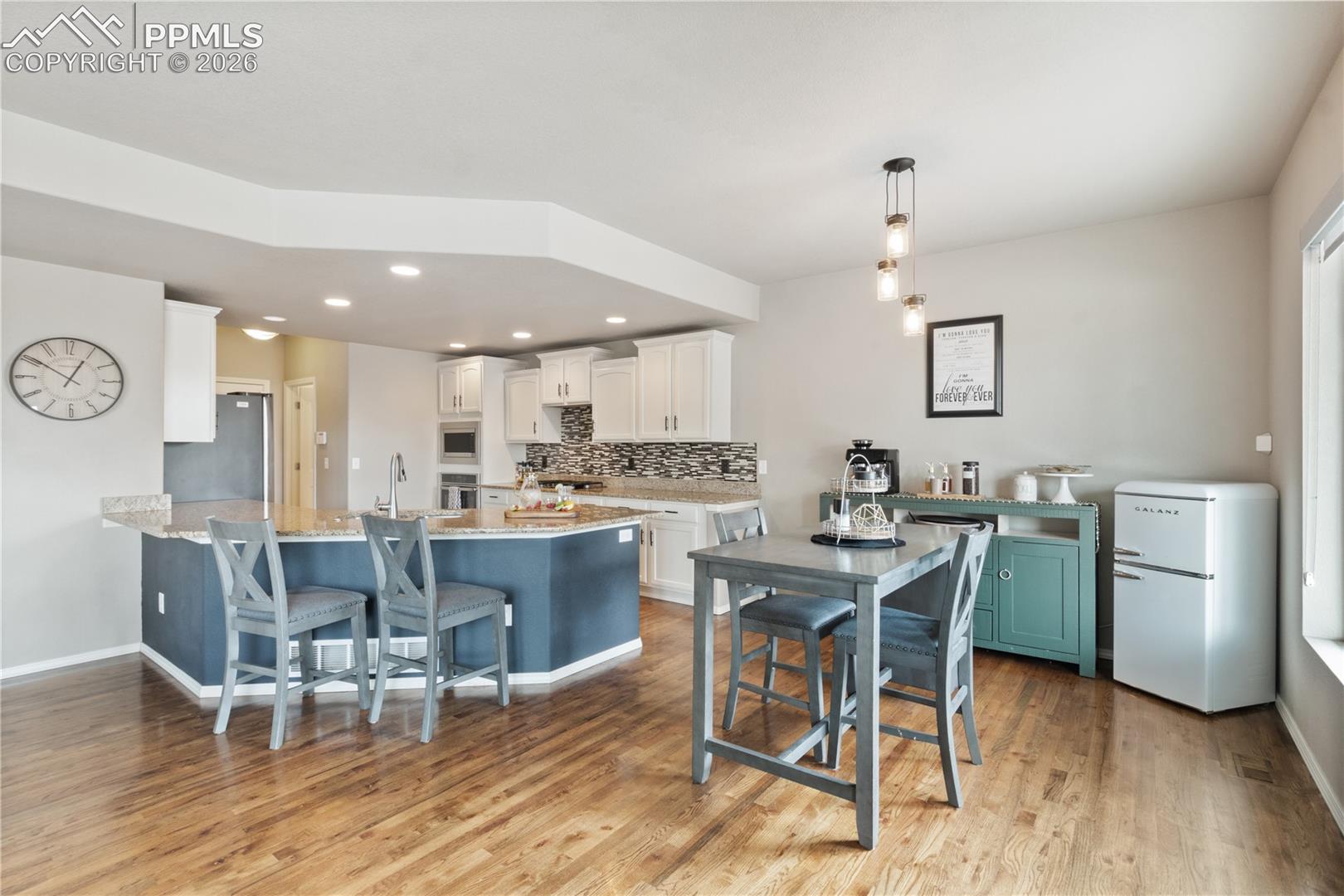 Kitchen with a kitchen breakfast bar, a peninsula, stainless steel appliances, white cabinetry, and light stone countertops