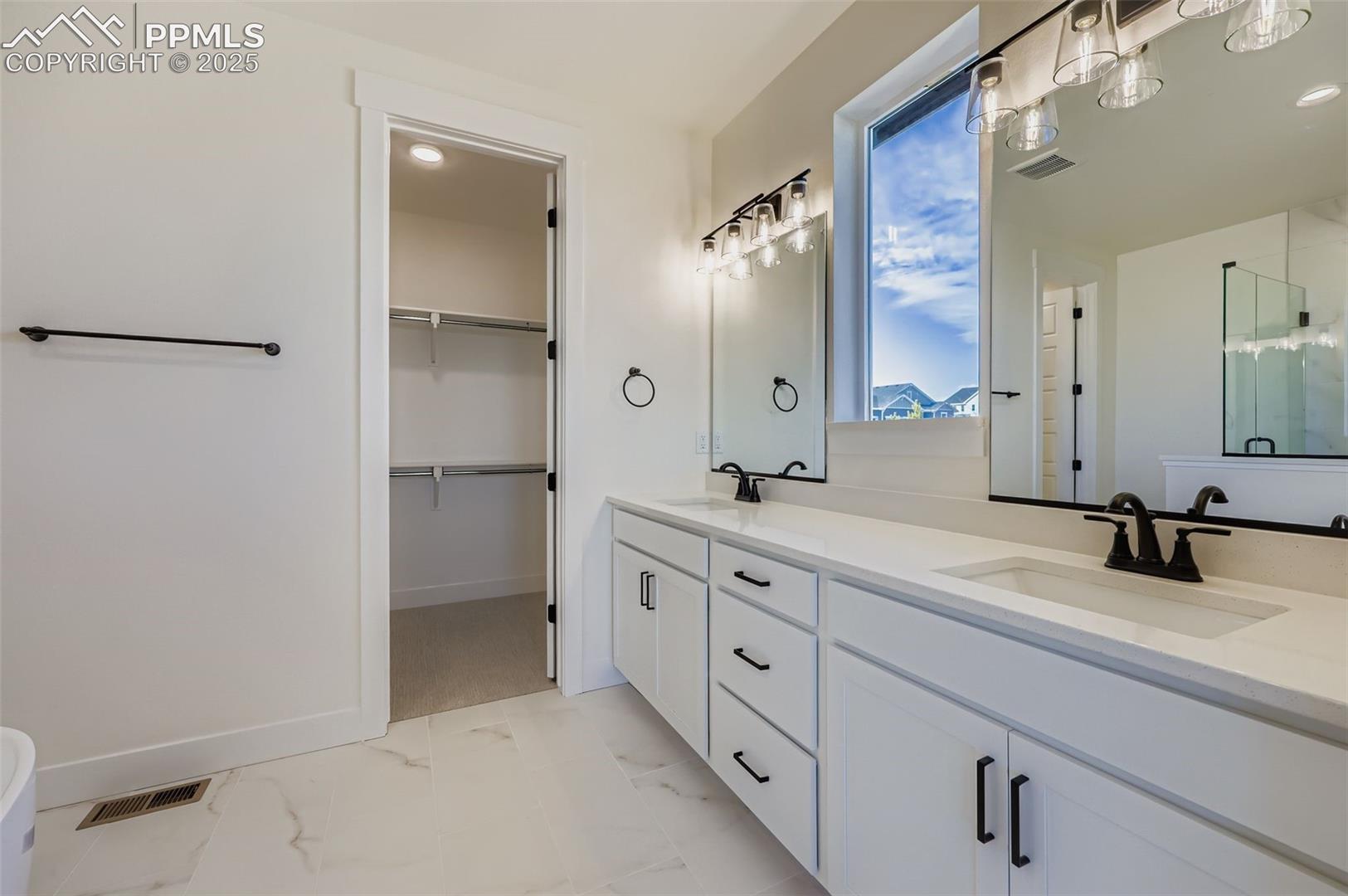 Full bath featuring double vanity, light marble finish floors, a walk in closet, recessed lighting, and a stall shower