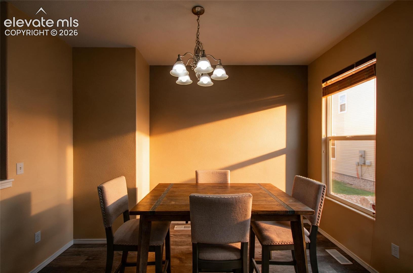 Five-light chandelier with frosted glass shades, single-hung window with wood blinds, and wood-finish flooring