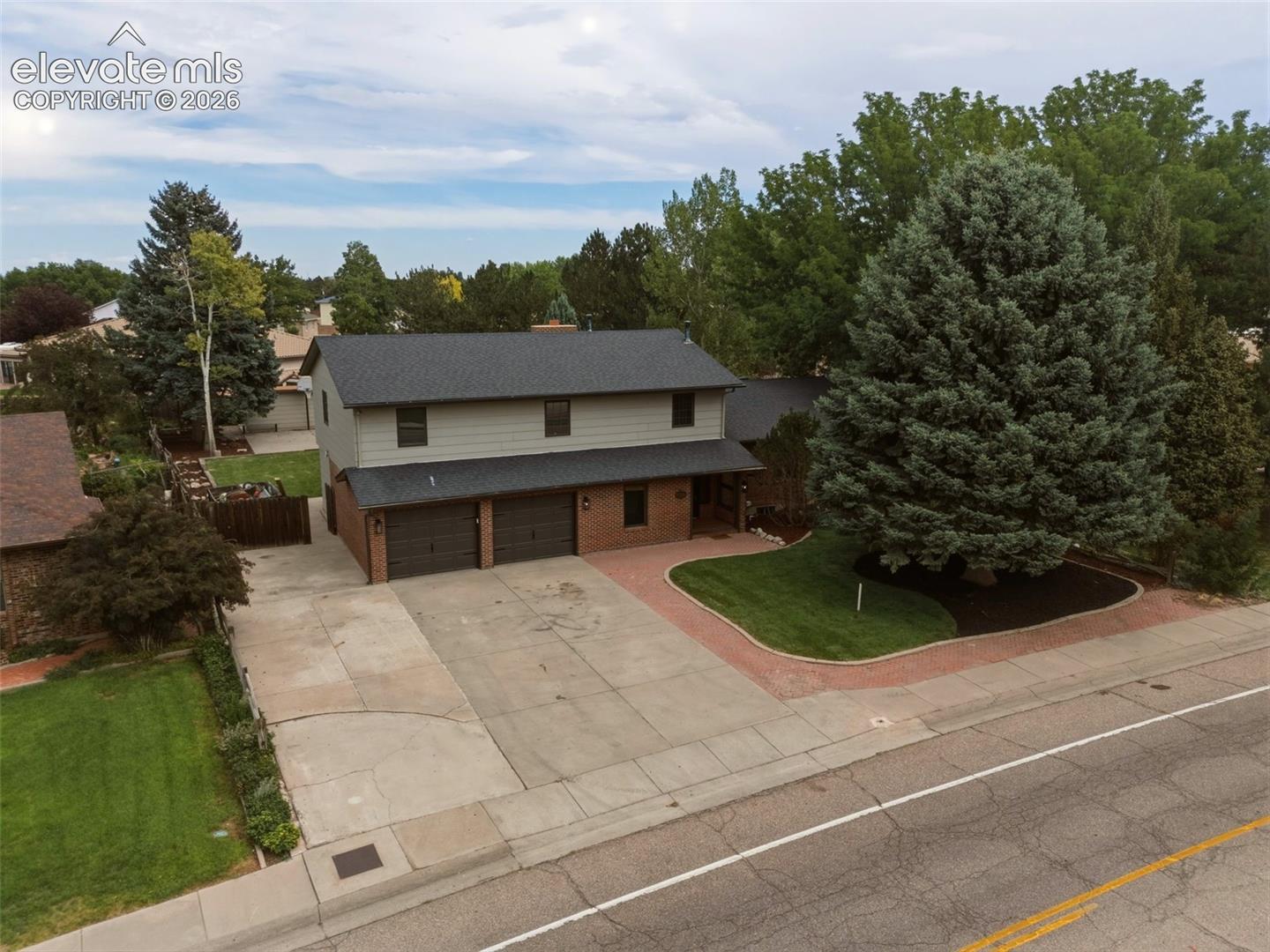 Two-story residence featuring a two-car garage, brick accents, and mature trees