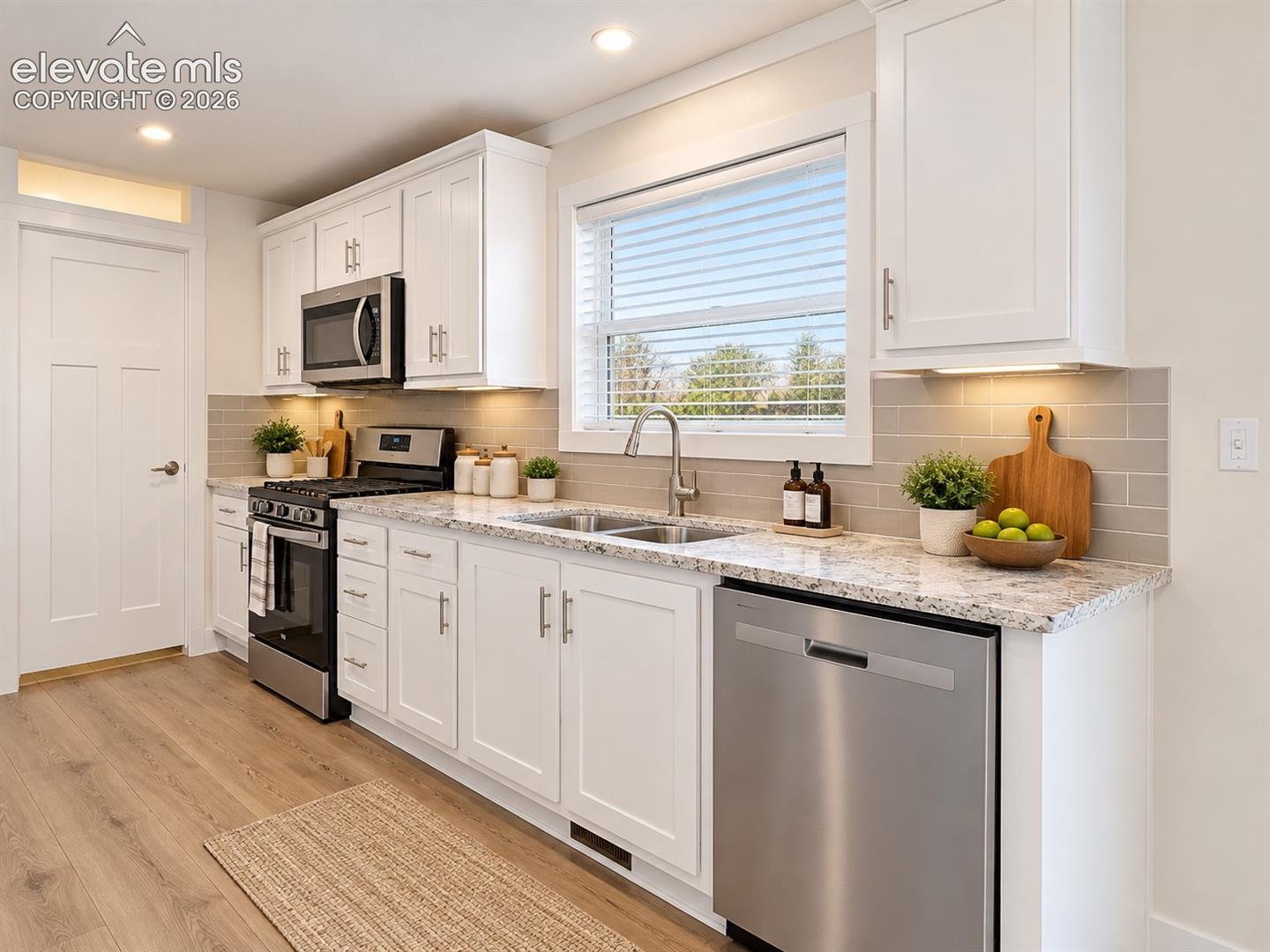 Kitchen – The kitchen's long counter run provides generous prep space and storage, complemented by shaker-style cabinetry, stainless steel appliances, and a tiled backsplash.