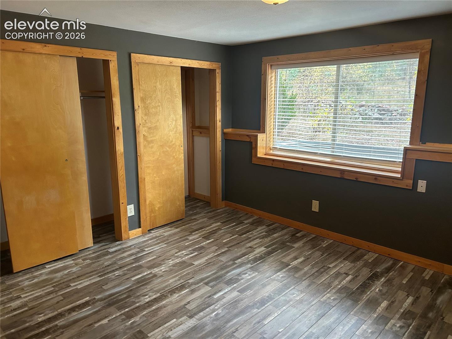 Room featuring wood-finish flooring, natural wood trim, sliding closet doors, and an inset window with integrated woodwork