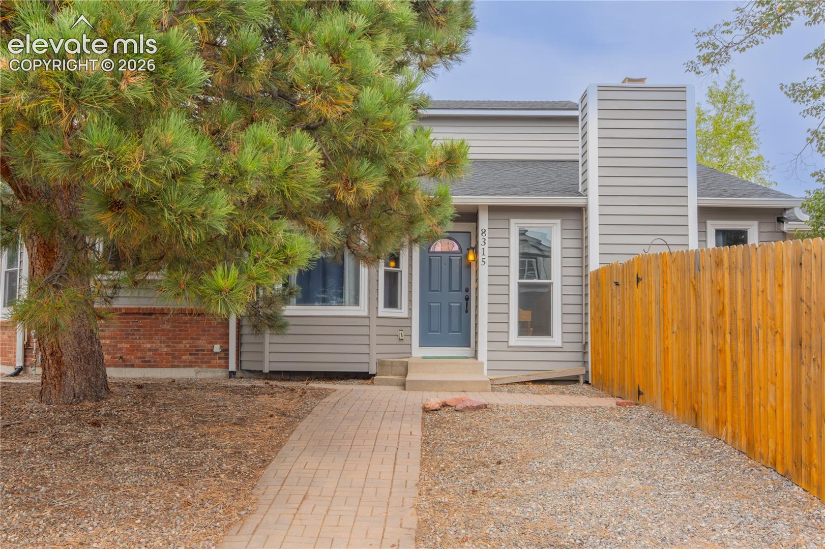 Light gray siding exterior with a dark blue entry door, a prominent chimney, and a full wood fence
