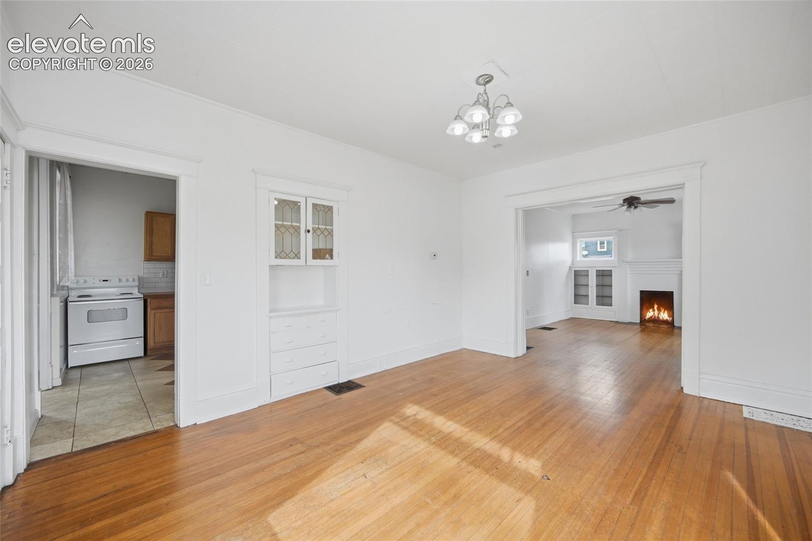 Hardwood flooring throughout, built-in recessed cabinetry with glass-panel doors, decorative multi-light chandelier, and fireplace mantel